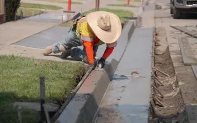 City employee working on cement and curb project along street.