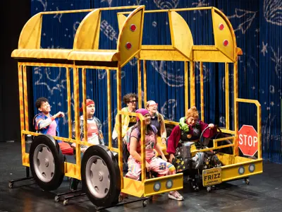Actors in "The Magic School Bus: Lost in the Solar System" appear in a yellow school bus on stage at the Cerritos Center for the Performing Arts.